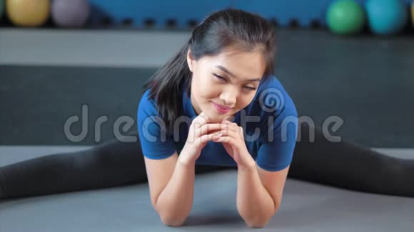微笑的亚洲女性普拉提教练坐在地上缠绕着看镜头的画像视频的预览图