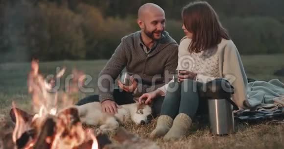 美丽浪漫的情侣在篝火旁的大自然中带着一只哈士奇狗一起喝茶视频的预览图