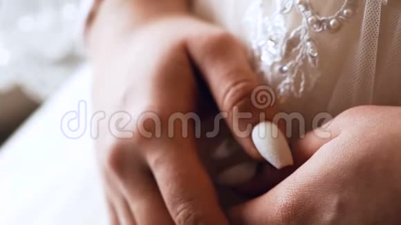 新娘的手在白色新娘的裙子上用简单而美丽的指甲特写视频的预览图
