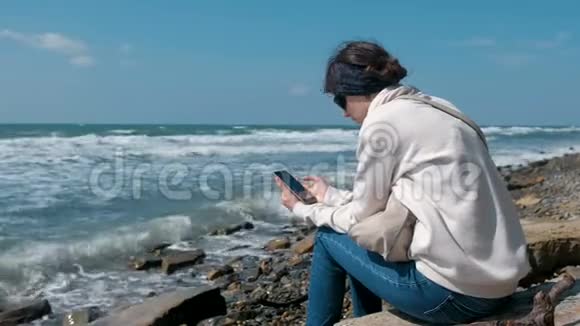 秋天女人坐在海边玩电话游戏视频的预览图