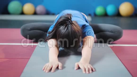 勤劳的亚洲年轻健身女坐在地毯上伸展双手视频的预览图
