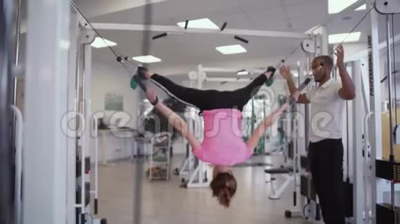教练帮助女性伸展她的身体挂在健身房的绳子上在健身房视频的预览图