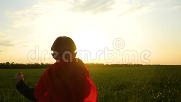 一个穿着超级英雄服装的孩子在夕阳的背景下穿过绿草视频的预览图