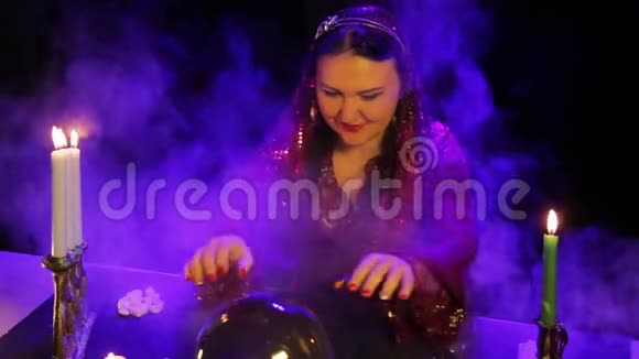 在烛光下的神奇沙龙里一个吉普赛人在烟雾中的镜球中读到未来视频的预览图