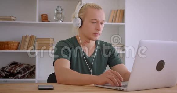 年轻英俊的金发时髦商人戴着耳机在办公室里用笔记本电脑特写肖像视频的预览图