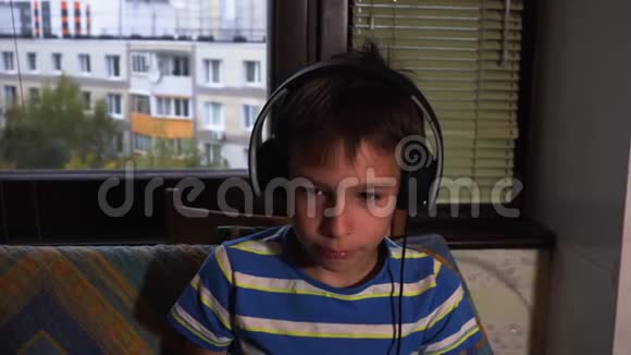 十几岁的男孩在家里用他的笔记本电脑笑着带着耳机看电影视频的预览图