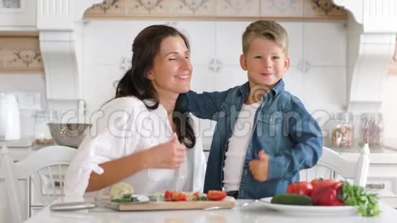 在家里的厨房里漂亮的妈妈和儿子拥抱着做着很酷的手势视频的预览图