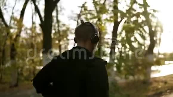平静的男人通过耳机跑步和听最喜欢的音乐早上在黑色绿色公园慢跑视频的预览图
