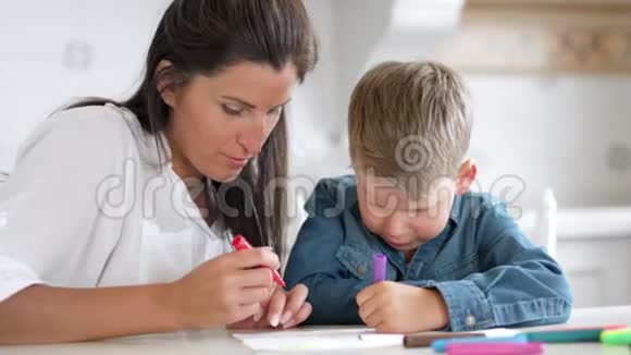 美丽的母亲帮助小儿子用彩色毡尖笔画形象视频的预览图