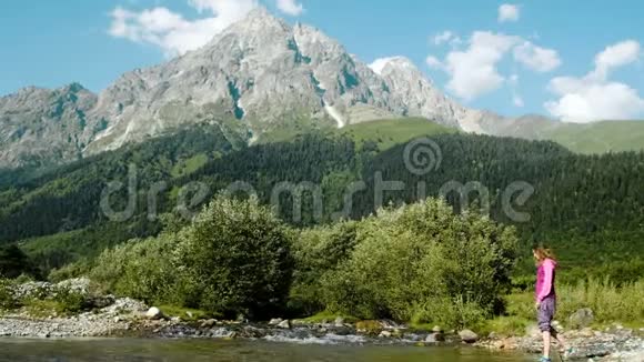 旅游女孩徒步旅行者走进一条小溪在山景的背景下洗手视频的预览图