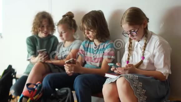 孩子和小玩意学校的孩子们拿着智能手机坐在学校的长凳上网瘾视频的预览图