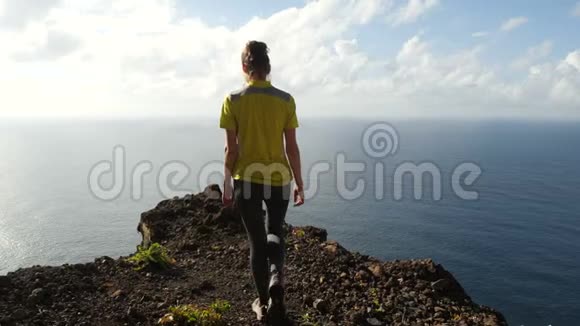 年轻女子举起双臂站在美丽的陡峭悬崖上在美丽的风景中登上顶峰的女士视频的预览图