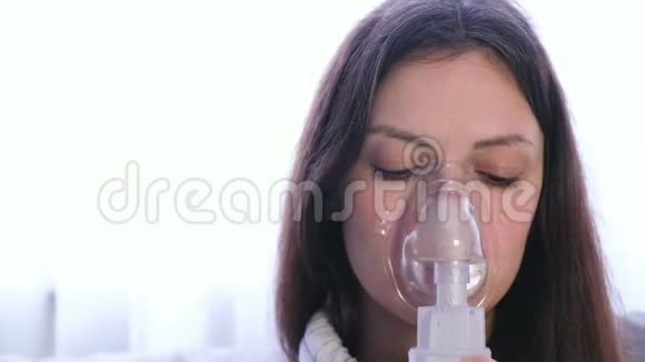 使用雾化器和吸入器进行治疗年轻女性通过吸入面罩吸入特写面部正面视图视频的预览图