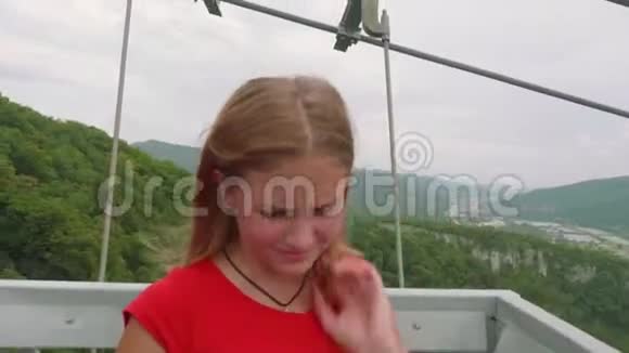年轻的白种人金发碧眼穿着红色t恤在山上背景下她使用黑色智能手机屏幕上的桥断了视频的预览图