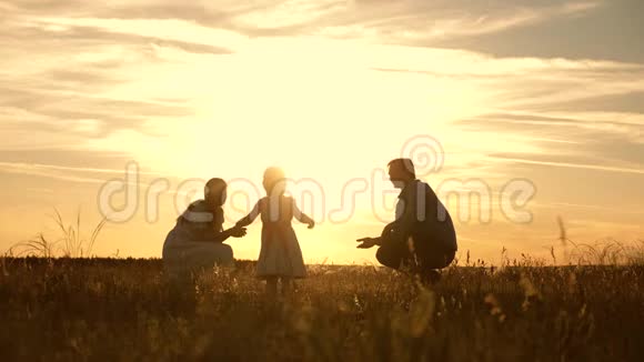 爸爸妈妈和他们的小女儿在公园里玩日落孩子迈出第一步一家人在玩视频的预览图