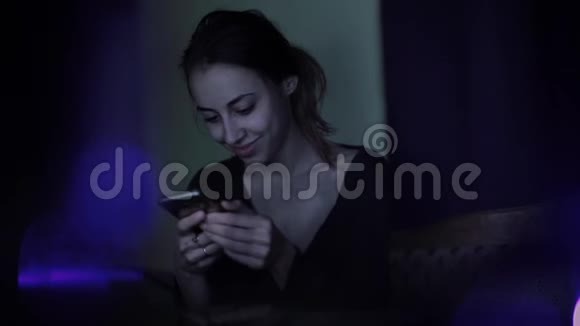 傍晚时分美丽微笑的女人坐在城市公园的草地上手里拿着一部电话一边刷卡一边看着留言视频的预览图
