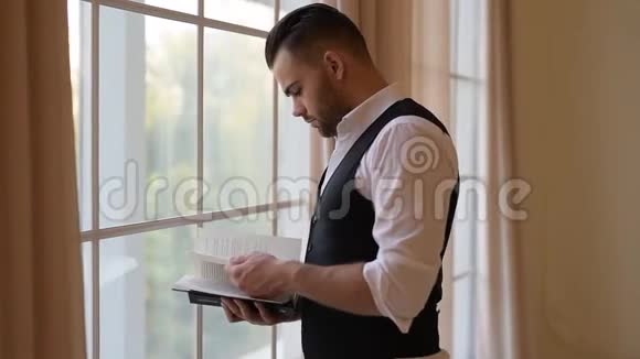 一个年轻人站在窗边翻书视频的预览图