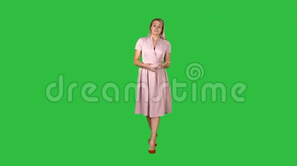 快乐的年轻女子穿着粉色连衣裙正走向相机在绿色屏幕上交谈Chroma键视频的预览图