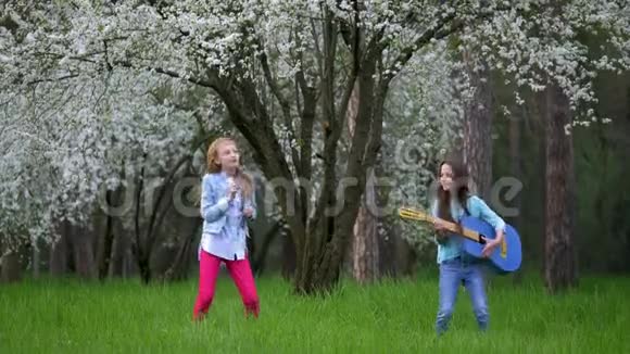 两个学校女朋友在春天的森林里上演了一场摇滚表演手里拿着吉他在跳着笑流动视频的预览图