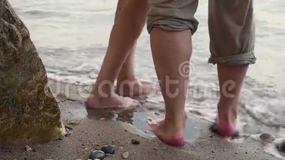 一对夫妇在晴朗的晴天沿着海滩散步他们牵手亲吻男人和女人的脚在视频的预览图