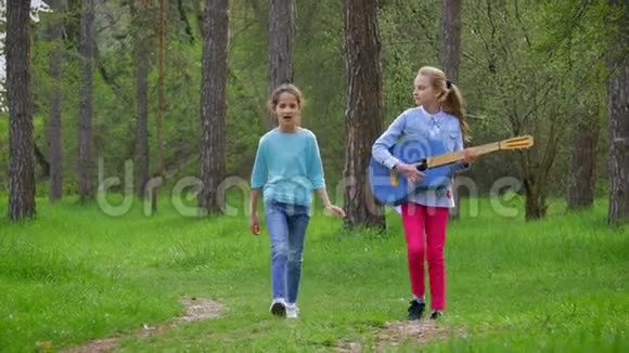 春天漫步在城市公园里两个带着吉他的白人小女孩在森林小径上玩耍视频的预览图