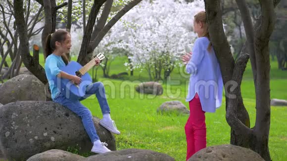 两个快乐的小女朋友在公园里弹吉他春天的音乐大自然美丽的田园风光视频的预览图