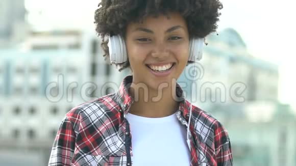 可爱的非裔美国女孩带着耳机看着相机微笑着快乐着视频的预览图