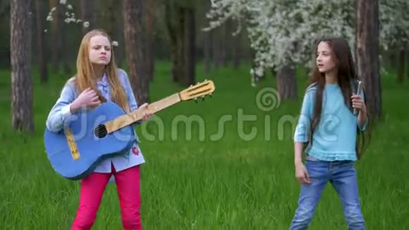 在森林公园里弹吉他音乐的小女孩跳舞使滑稽的脸傻瓜快乐的春天假期视频的预览图