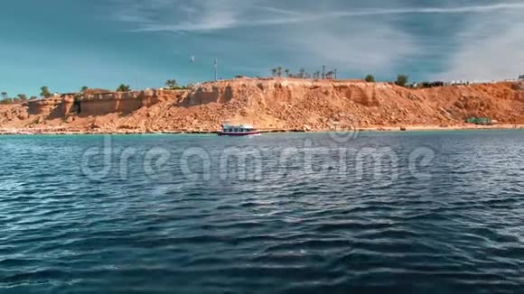 游船在蔚蓝的海面上行驶在岩石海岸的背景下海滩是黄色的视频的预览图