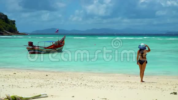 一个女孩站在海滩上看着一艘传统的泰国长尾船视频的预览图