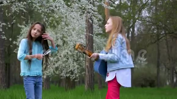 可爱的少女女友在户外弹吉他小女孩一起唱歌梳头跳舞视频的预览图