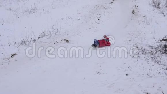 快乐的女孩在冬天白雪皑皑的雪橇上从雪山上滚下来微笑着圣诞节假期慢动作视频的预览图