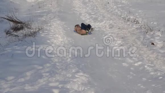 女孩在雪橇上翻滚从一个高雪覆盖的滑梯女孩冬天在公园里玩慢动作视频的预览图