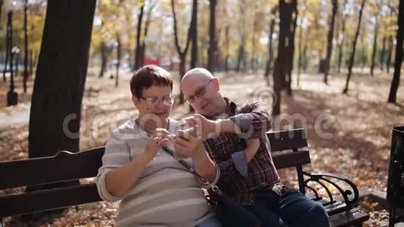 秋天公园里的一对老夫妇用智能手机浏览照片和上网视频的预览图