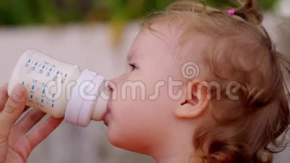 蓝眼睛的小漂亮女孩从瓶子里喝牛奶孩子自己拿着瓶子视频的预览图