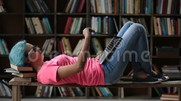 一个可爱的女孩手提电脑躺在图书馆的长凳上视频的预览图