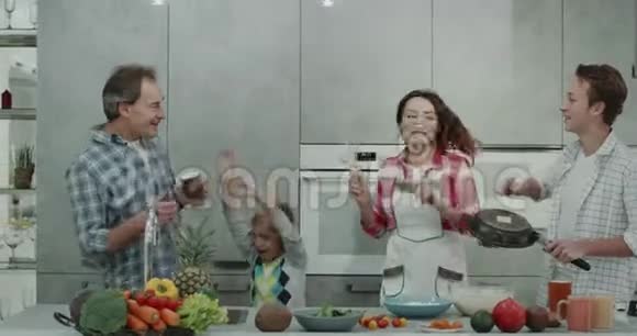 有趣的一家人在一个现代化的厨房里共度一个美好的早晨用一个平底锅一个手动搅拌器和两个男孩玩视频的预览图
