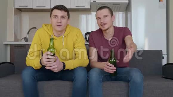 两个人坐在沙发上看电视上的足球赛喝啤酒评论视频的预览图