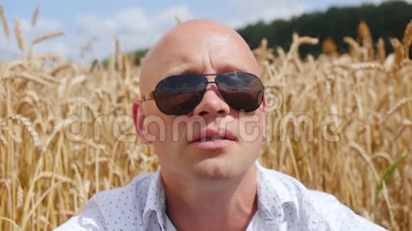 背景麦田上戴着太阳镜的秃头男人的肖像看着对着镜头唱歌关门视频的预览图