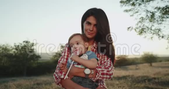 年轻的母亲抱着儿子看着大自然看着镜头特写小男孩拿着一个大棒棒糖缓慢的动作视频的预览图