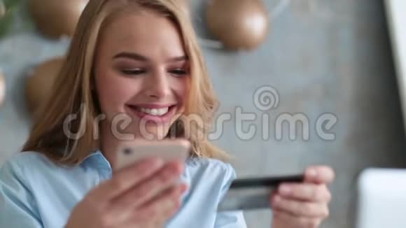 优雅的金发女人坐在办公室拿着手机和塑料卡在网站上注册视频的预览图