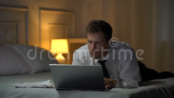 体贴的男性躺在床上在笔记本电脑上阅读文件商务电子邮件视频的预览图