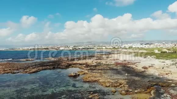 海浪冲击岩石海滩的无人机海岸景背景中的山脉和城市建筑塞浦路斯帕福斯岛视频的预览图