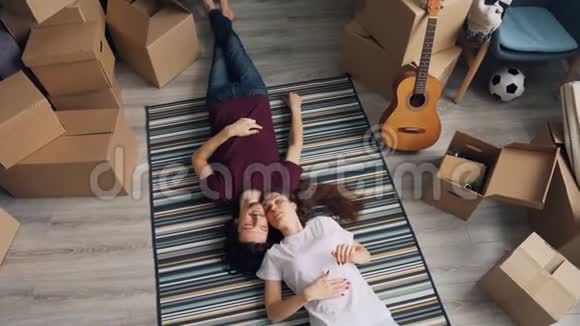 幸福的男人和女人在新的公寓里躺在地毯上与盒子交谈的最高景观视频的预览图