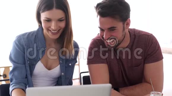 漂亮可爱的年轻夫妇用笔记本电脑在家里的厨房里聊天视频的预览图
