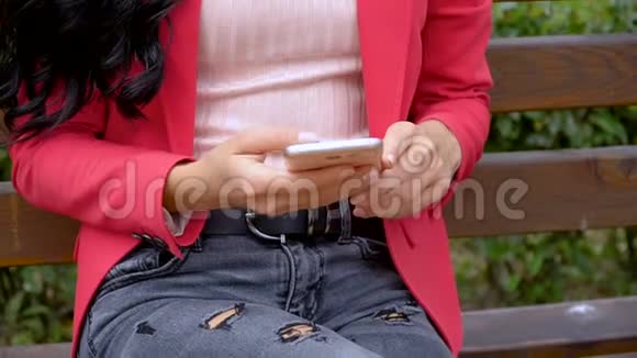 一个坐在长凳上的城市公园里用智能手机的女孩一头棕色长发视频的预览图