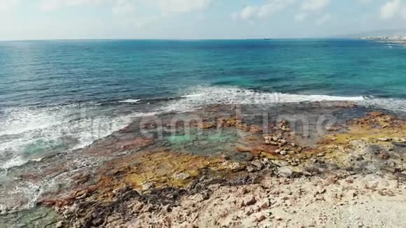 空中拍摄的蓝色海洋和岩石海滩海岸海浪拍打岩石塞浦路斯帕福斯海岸线无人机视图视频的预览图