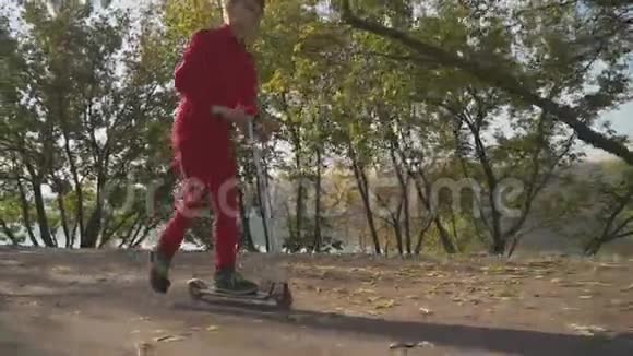 穿红色衬衫和裤子的小男孩在公园里骑滑板车这孩子积极地把时间花在户外慢动作视频的预览图