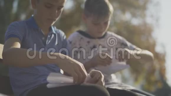 两个小男孩在户外做纸飞机孩子们坐在公园的长凳上视频的预览图