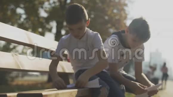 两个男孩在户外做纸飞机孩子们坐在公园的长凳上视频的预览图